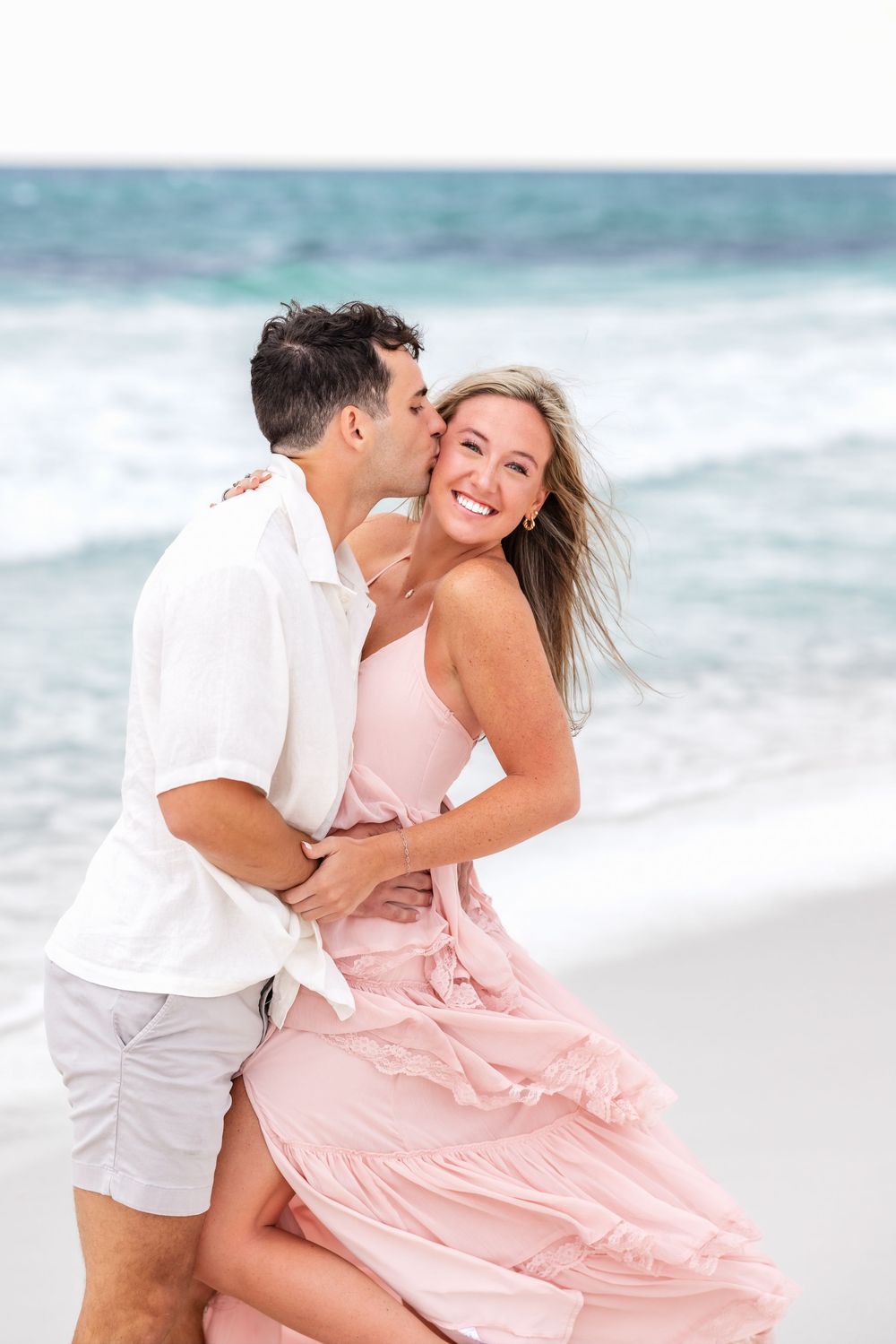 Romantic couple sharing intimate moments on a scenic beach with turquoise waters in the background.
