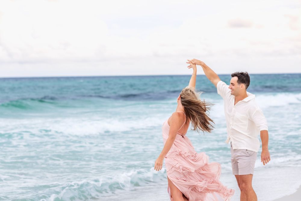 Couple walking hand in hand on a sunny white sand beach with ocean waves in the background.