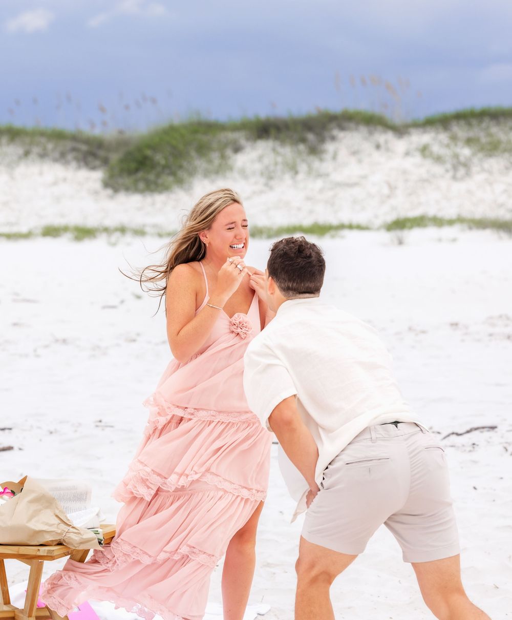A couple in beachwear playfully runs along white sandy dunes on a sunny day.