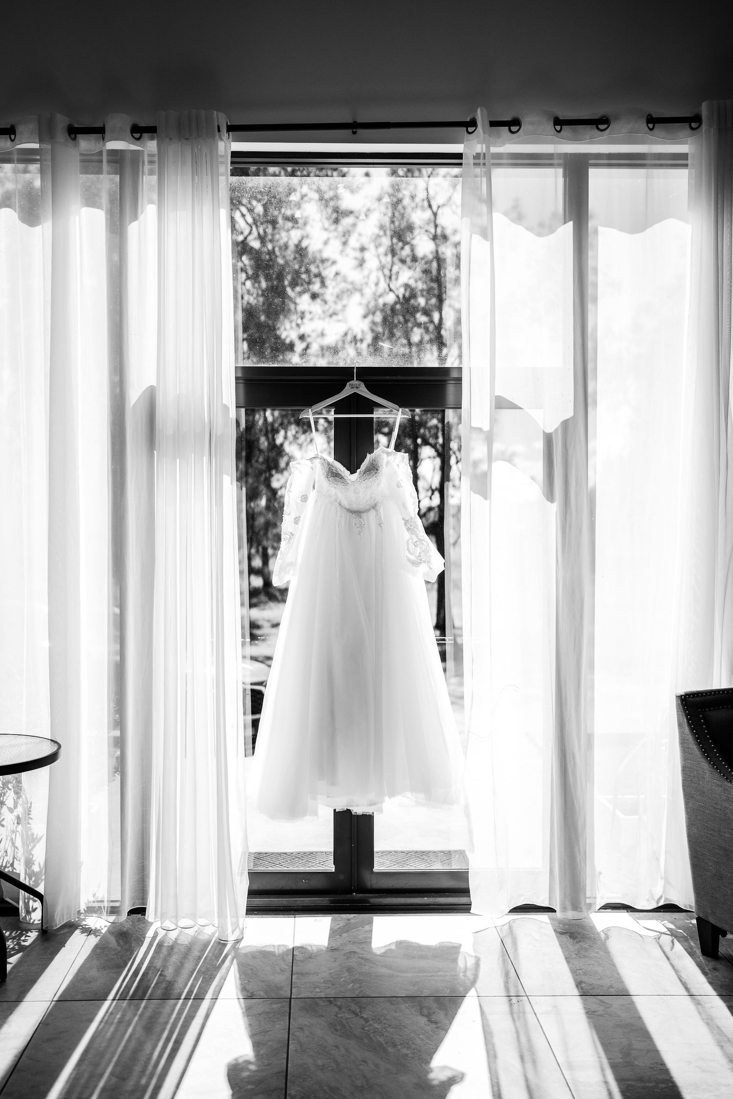 White dresses and garments hanging elegantly in a row against backlit windows creating a dreamy silhouette effect.