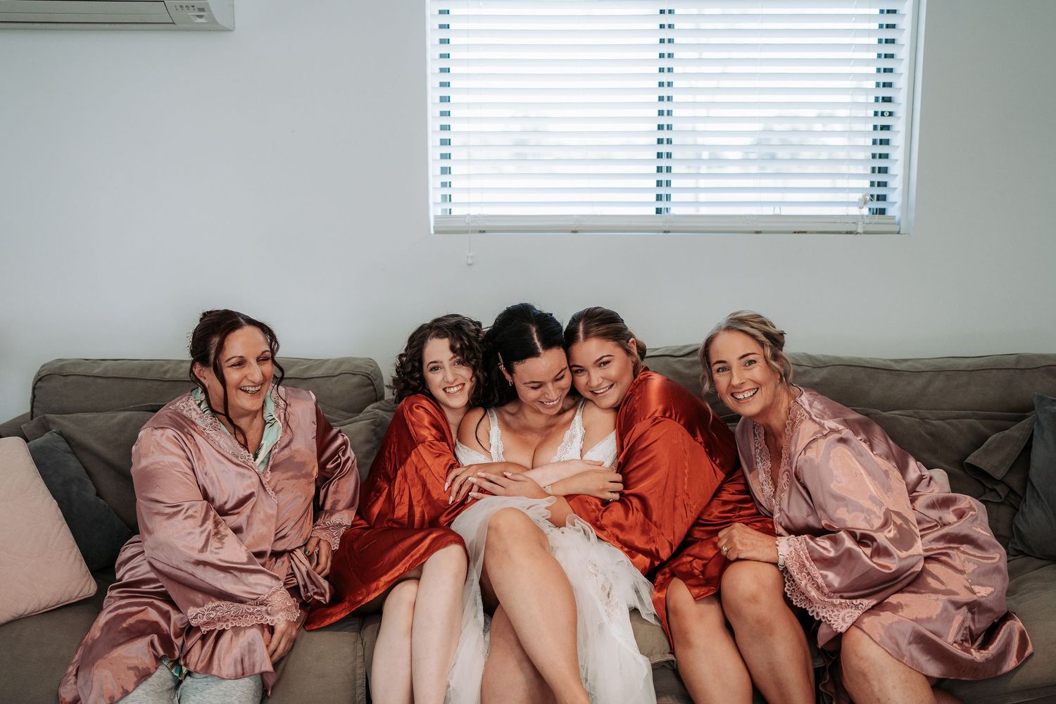 Group of friends lounging on a gray couch together wearing cozy robes while looking at their phones.