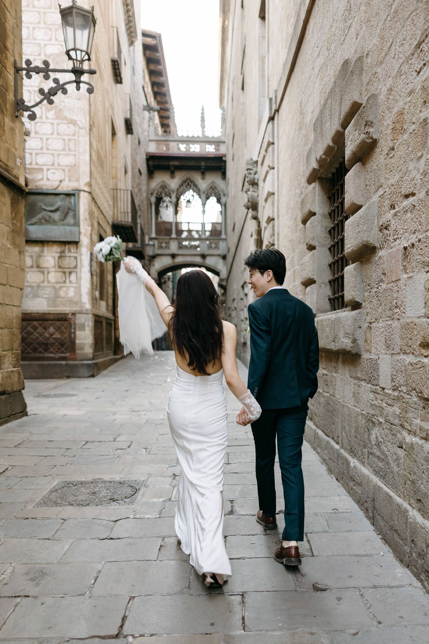 Couple walking down a historic stone alleyway in formal wedding attire.