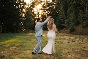 A couple walking hand in hand through a meadow at sunset with golden light filtering through the trees.