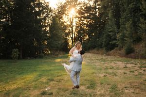 A person twirling in a flowing white dress at sunset in a grassy meadow with evergreen trees in the background.