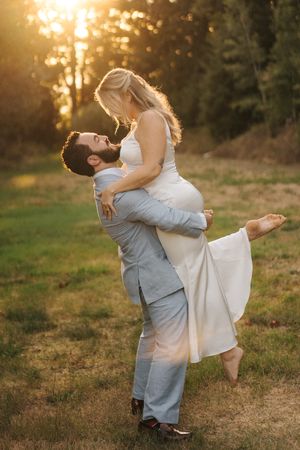 A couple embraces in a romantic sunset photo shoot, with the bride lifting her leg in an elegant white dress and groom in gray suit.
