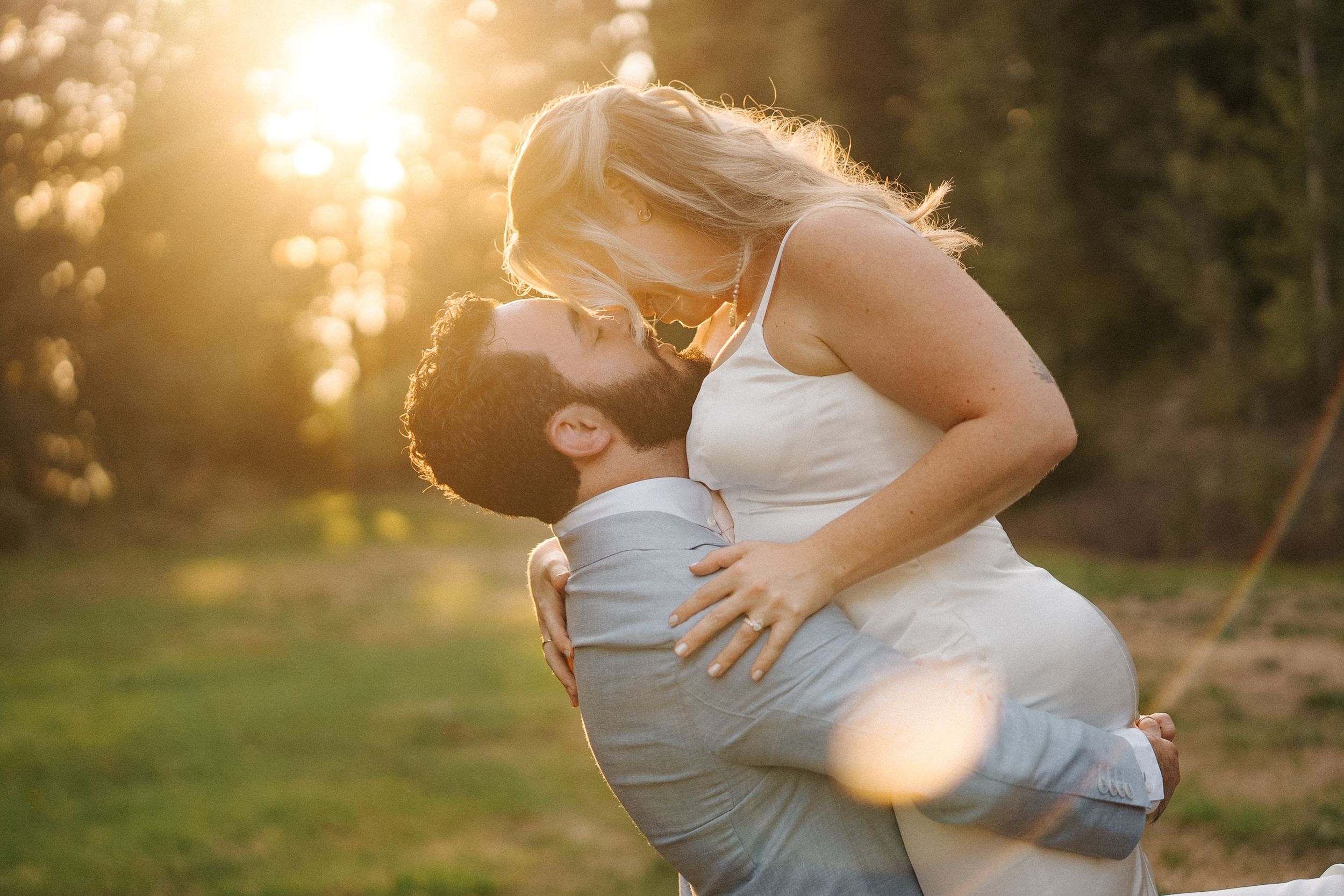 A romantic couple embraces in a beautiful golden sunset, with sun flares adding a dreamy atmosphere to their intimate moment.