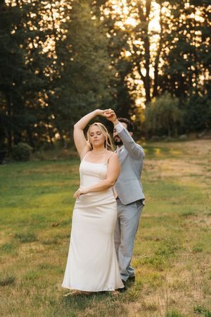 Couple dancing together at sunset in a grassy meadow during golden hour.