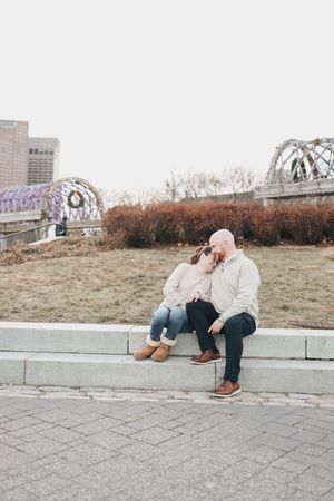 A couple sits together on concrete steps in an urban setting during a casual outdoor photoshoot.
