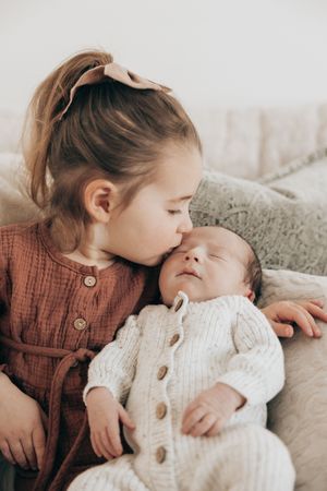 Sweet tender moment as person in brown clothing snuggles with baby in white knit outfit on cozy blankets.