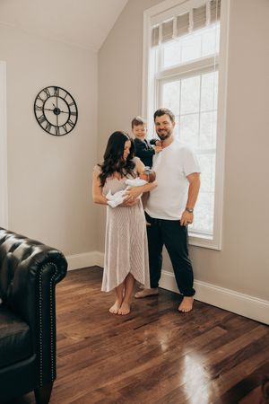 A couple in white clothing shares intimate poses against a wall in a minimalist room with hardwood floors.