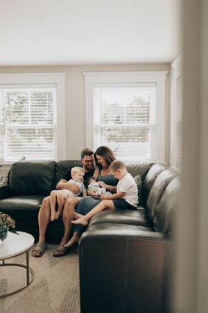 A peaceful scene shows a family relaxing together on a dark leather sectional sofa in a bright, modern living room.