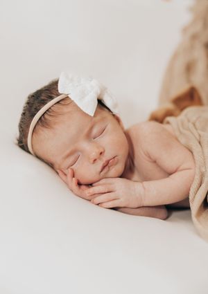 A sleeping newborn in a soft cream-colored setting with delicate white headband captured in minimalist style.