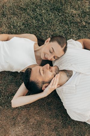 A couple in white clothing lying on grass together sharing an intimate moment outdoors.