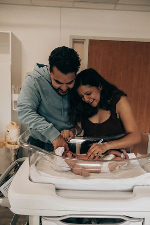 A couple smiles while leaning over a changing table and tending to their baby together.