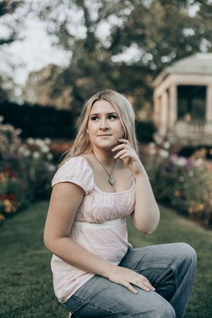 A person in a pink top and jeans sits casually outdoors in a garden setting with soft lighting and bokeh effects.