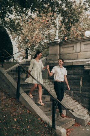A couple descending stone steps in autumn, with fall foliage in the background creating a romantic vintage atmosphere.