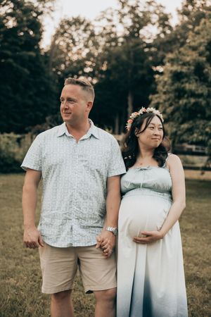 A couple poses in coordinating white and beige outfits in a natural outdoor setting during a photo session.