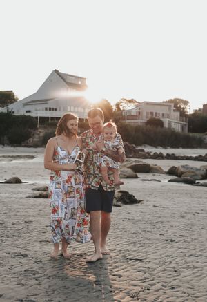 People in matching outfits enjoy a sunset photoshoot at a beach with buildings and palm trees in the background.