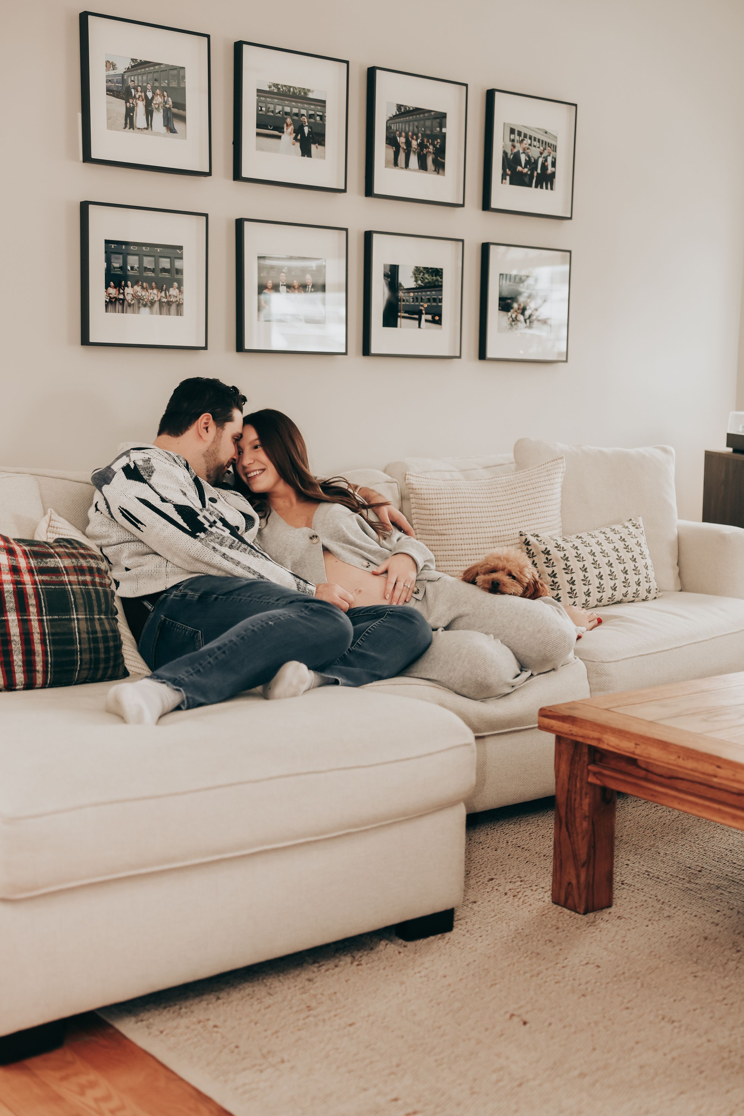 A couple relaxes together on a white sectional sofa in a cozy living room with framed photos on the wall.
