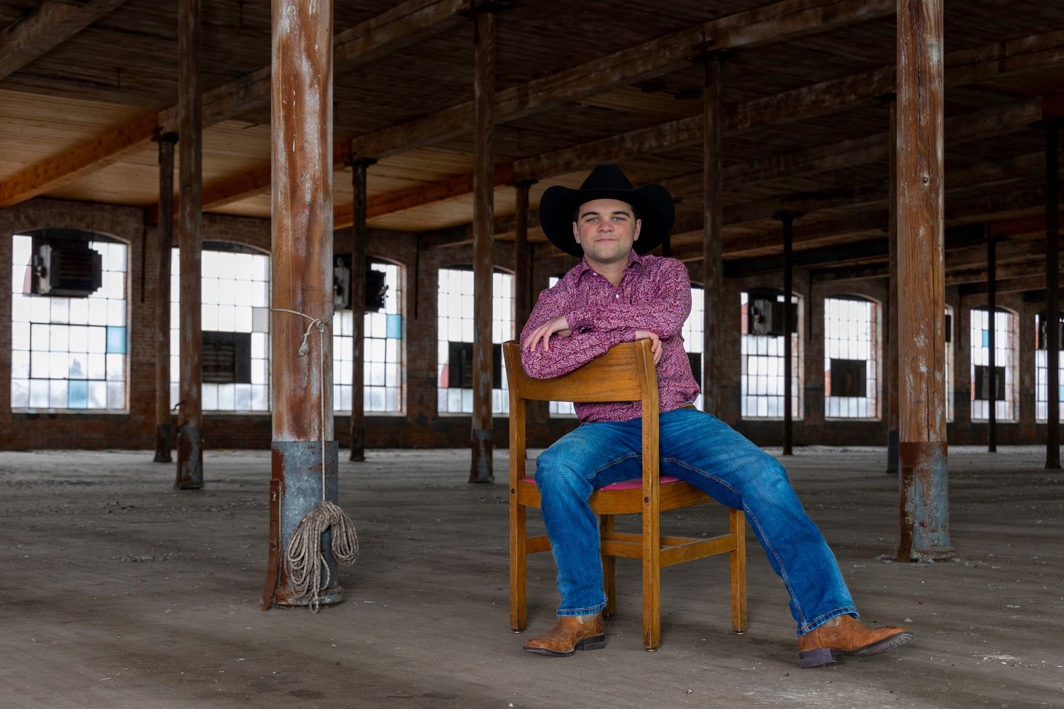Workers in cowboy boots walk through a large empty warehouse space with exposed wooden beams and supports.