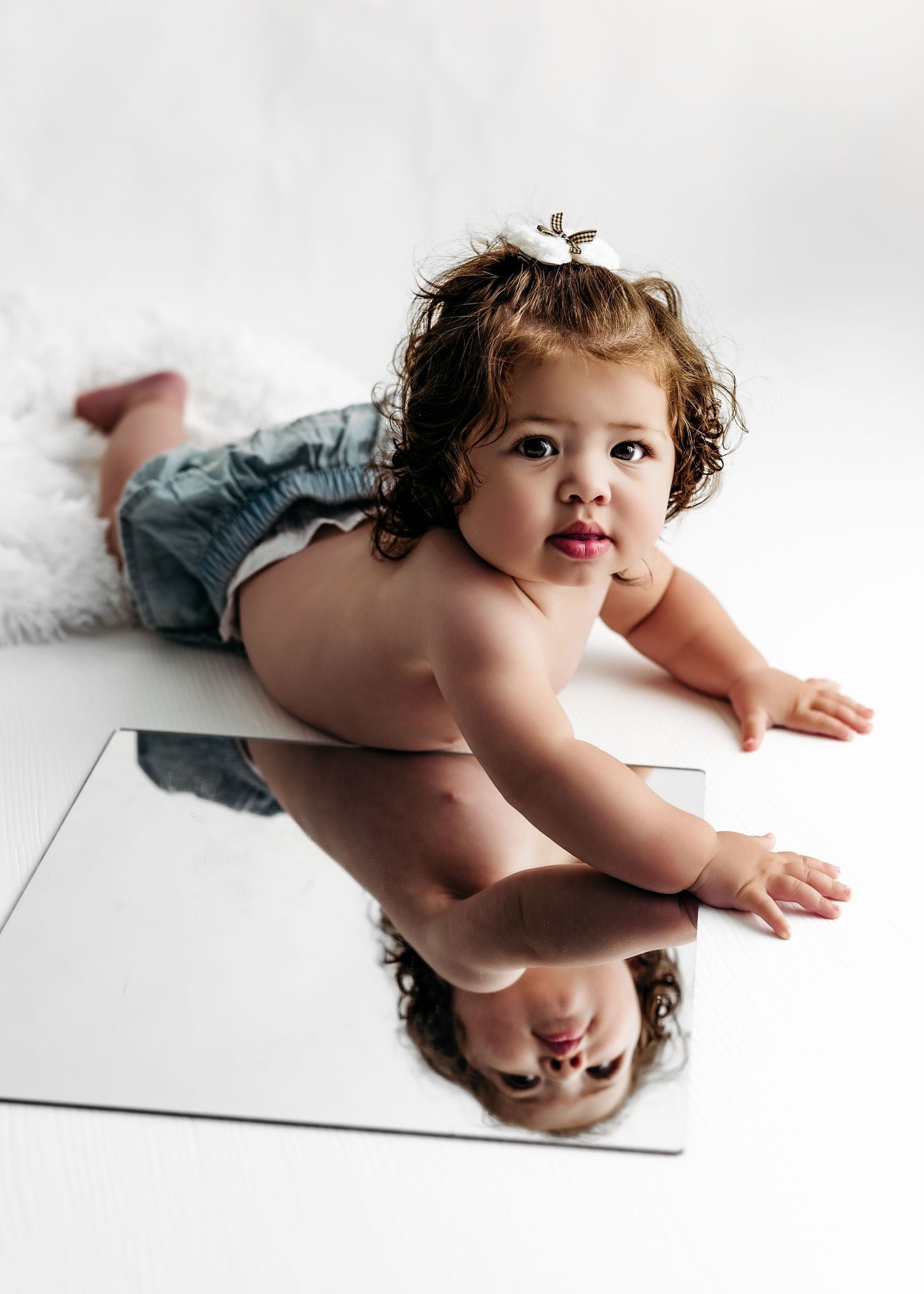 A tiny baby with curly hair explores their reflection in multiple angled mirrors creating a kaleidoscope effect.