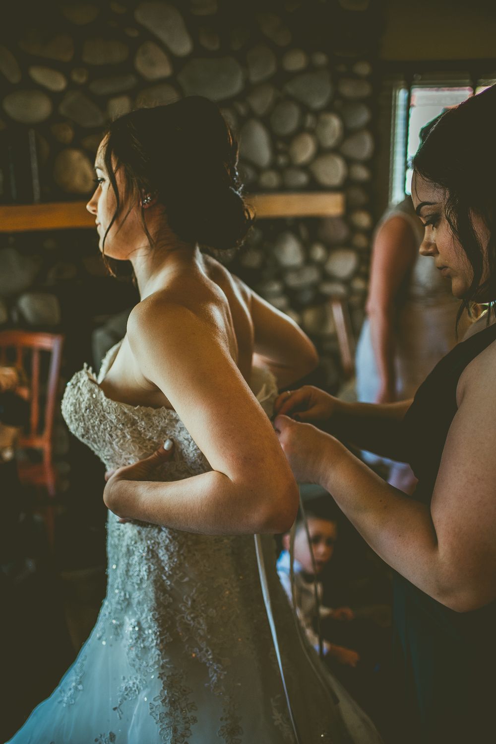 Getting ready scene of the wedding dress being laced up in a rustic stone wall venue. Banff Micro Wedding Photographer