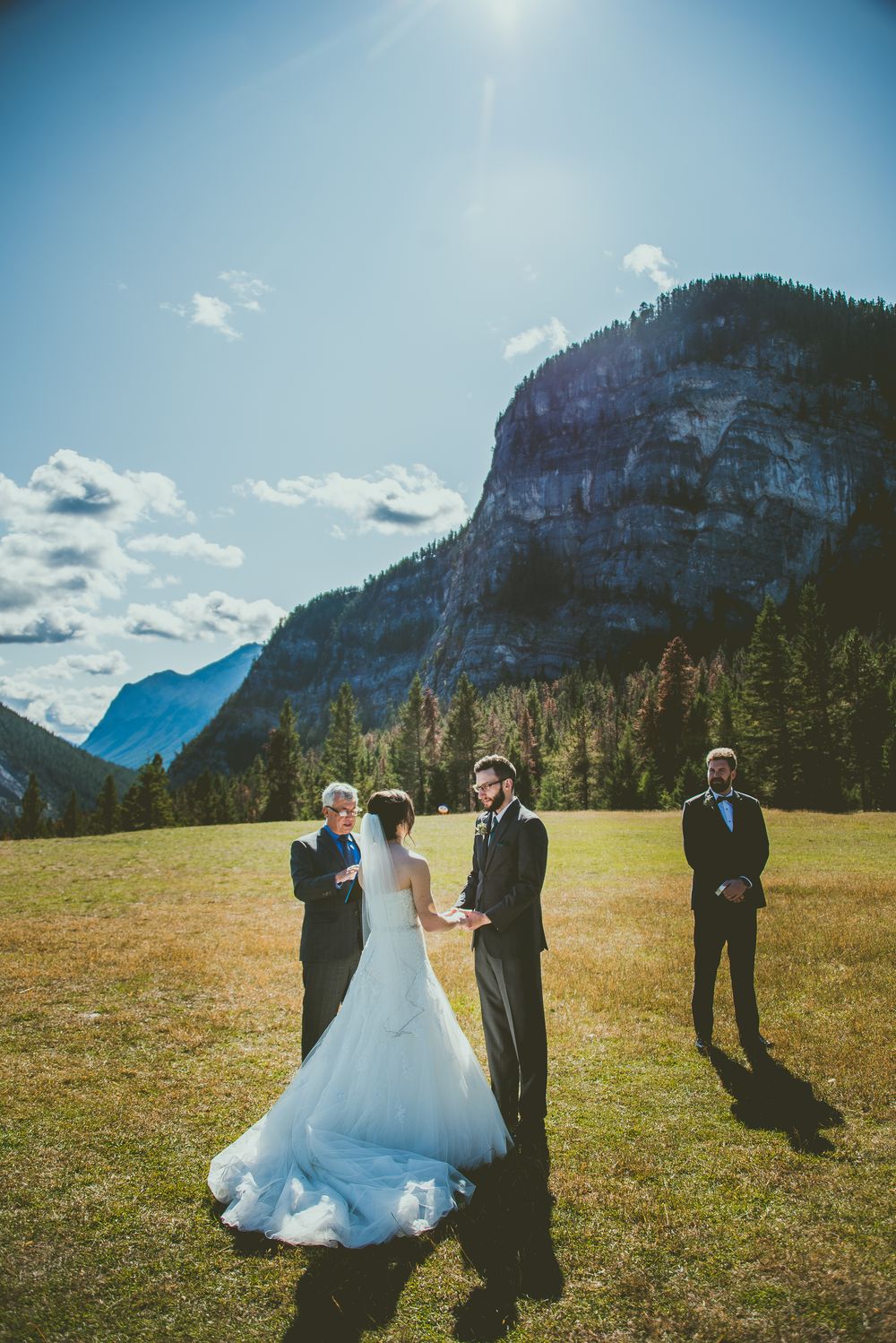 A wedding ceremony takes place in a scenic mountain meadow with dramatic cliffs and blue skies Banff Micro Wedding Photographer
