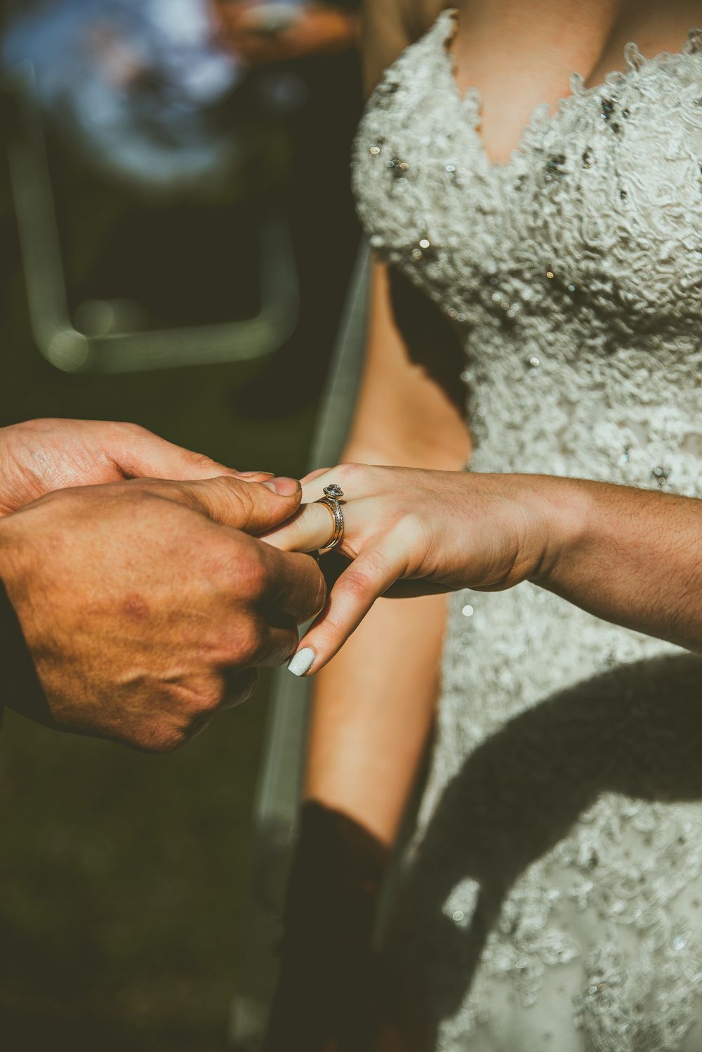Close-up of hands placing an engagement ring during an outdoor wedding ceremony, with a white lace dress Banff Micro Wedding Photographer
