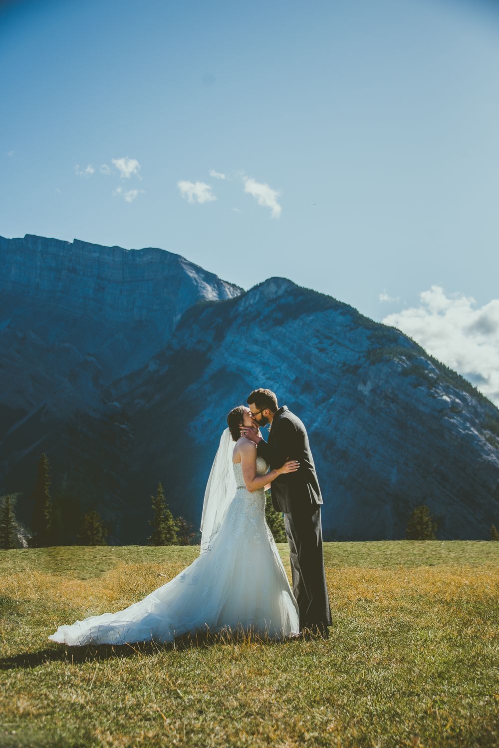 A romantic outdoor wedding moment against stunning mountain scenery with sunlit meadows and blue skies. Banff Micro Wedding Photographer