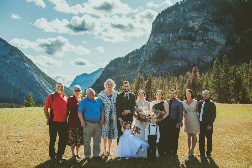 Group photo against stunning mountain backdrop in Banff with evergreen trees and cloudy skies. Banff Micro Wedding Photographer