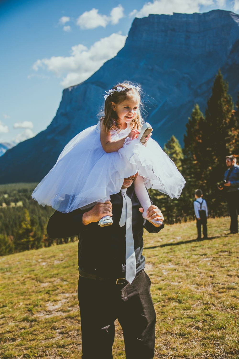 Playful wedding moment on a grassy mountainside with dramatic peaks and blue skies in the background. Banff Micro Wedding Photographer