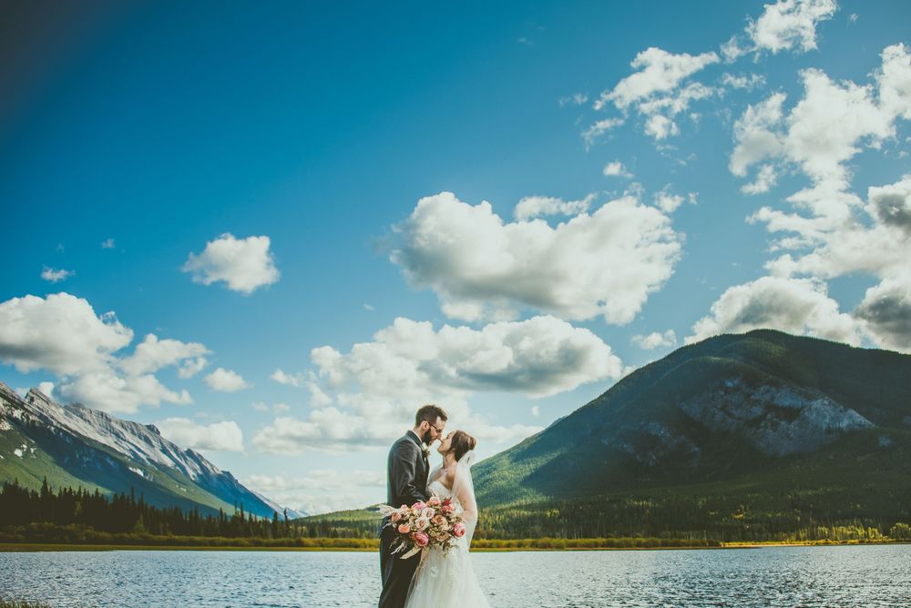 Panoramic mountain wedding portraits with dramatic clouds and blue skies over a lake. Banff Micro Wedding Photographer