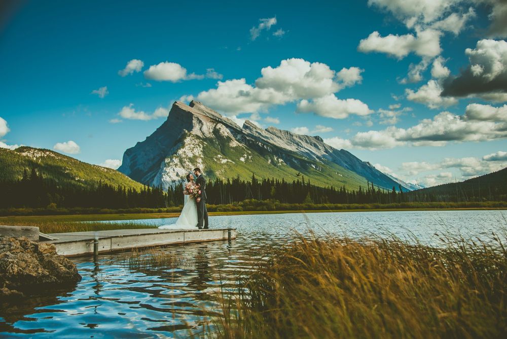 Scenic mountain lake wedding photos with dramatic clouds and snow-capped peaks in the background. Banff Micro Wedding Photographer