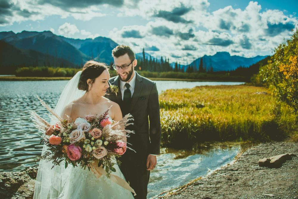 Wedding couple poses by mountain lake surrounded by vibrant wildflowers and dramatic peaks. Banff Micro Wedding Photographer