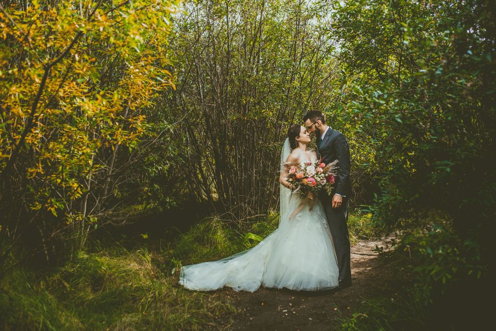 A romantic outdoor wedding photo with a couple surrounded by vibrant yellow forsythia and green foliage. Banff Micro Wedding Photographer