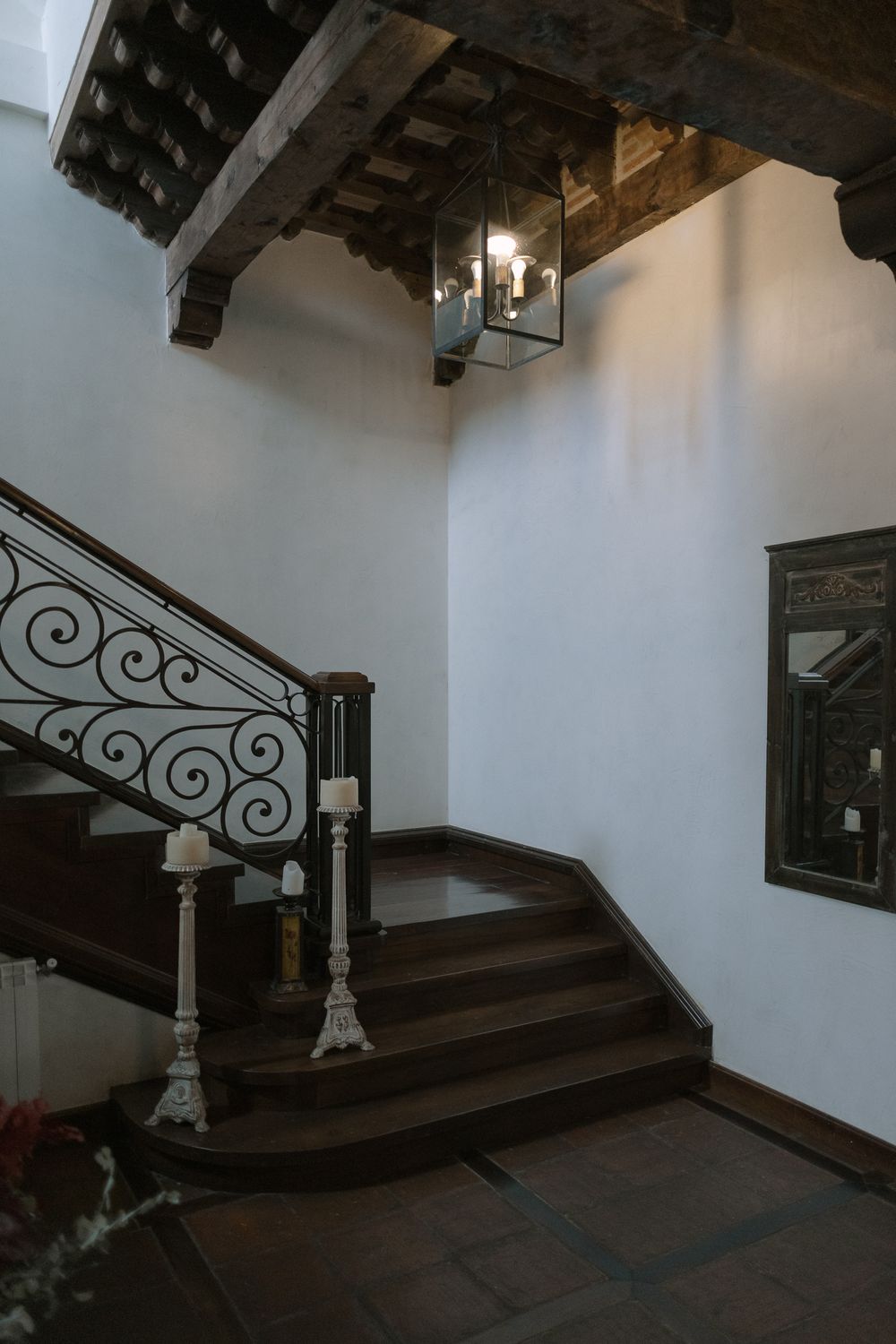 Elegant dark wood staircase with ornate wrought iron railings and candle holders under exposed wooden beam ceiling.