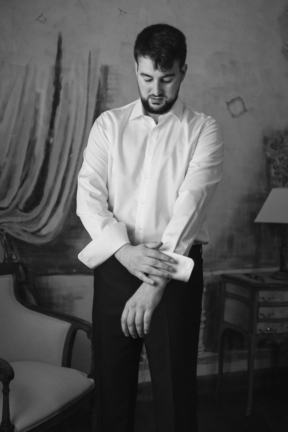Black and white portrait of someone in a formal white dress shirt and dark pants adjusting their sleeve.