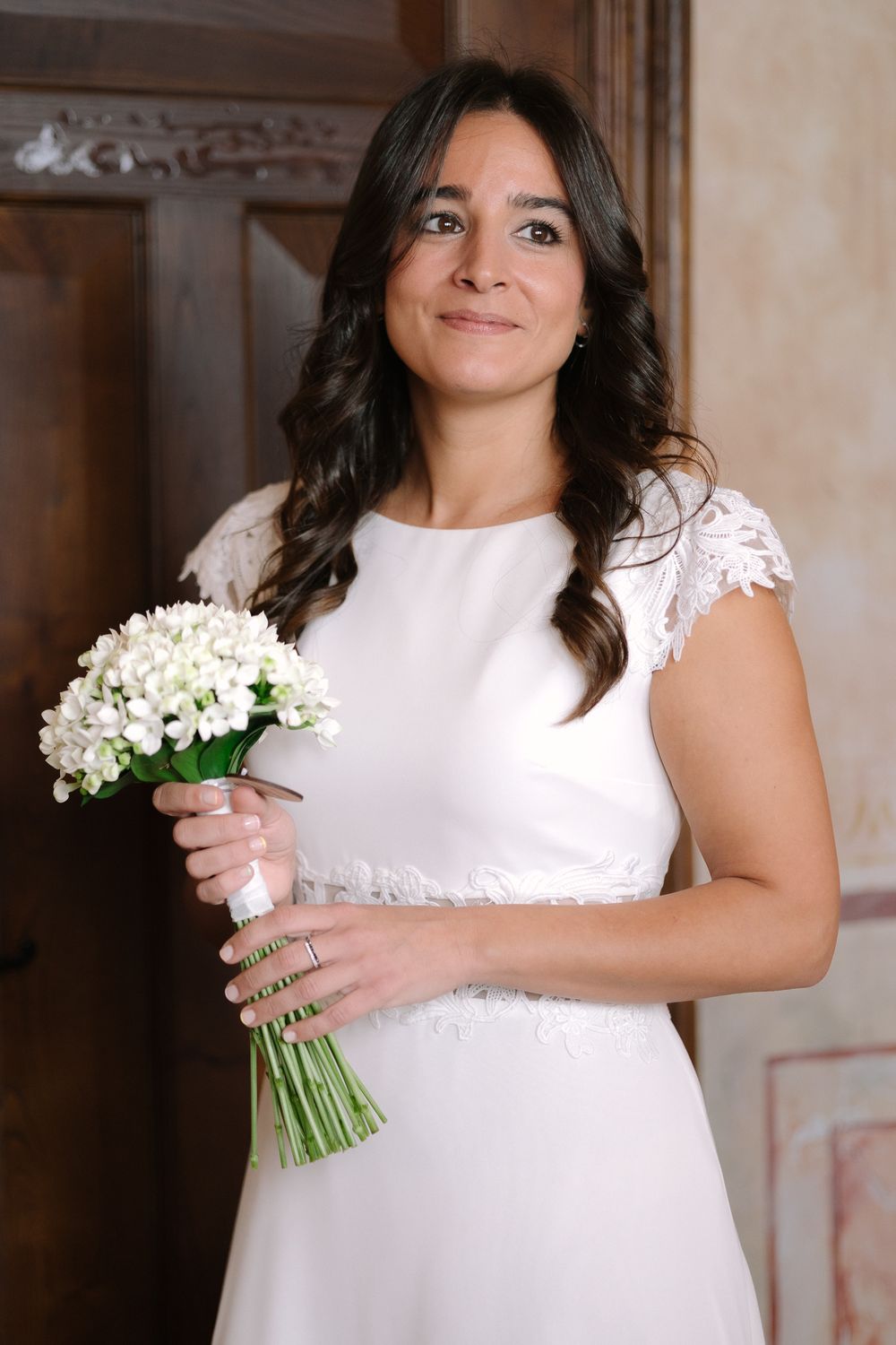 Wedding portrait showing elegant white dress with lacy cap sleeves and small white floral bouquet.