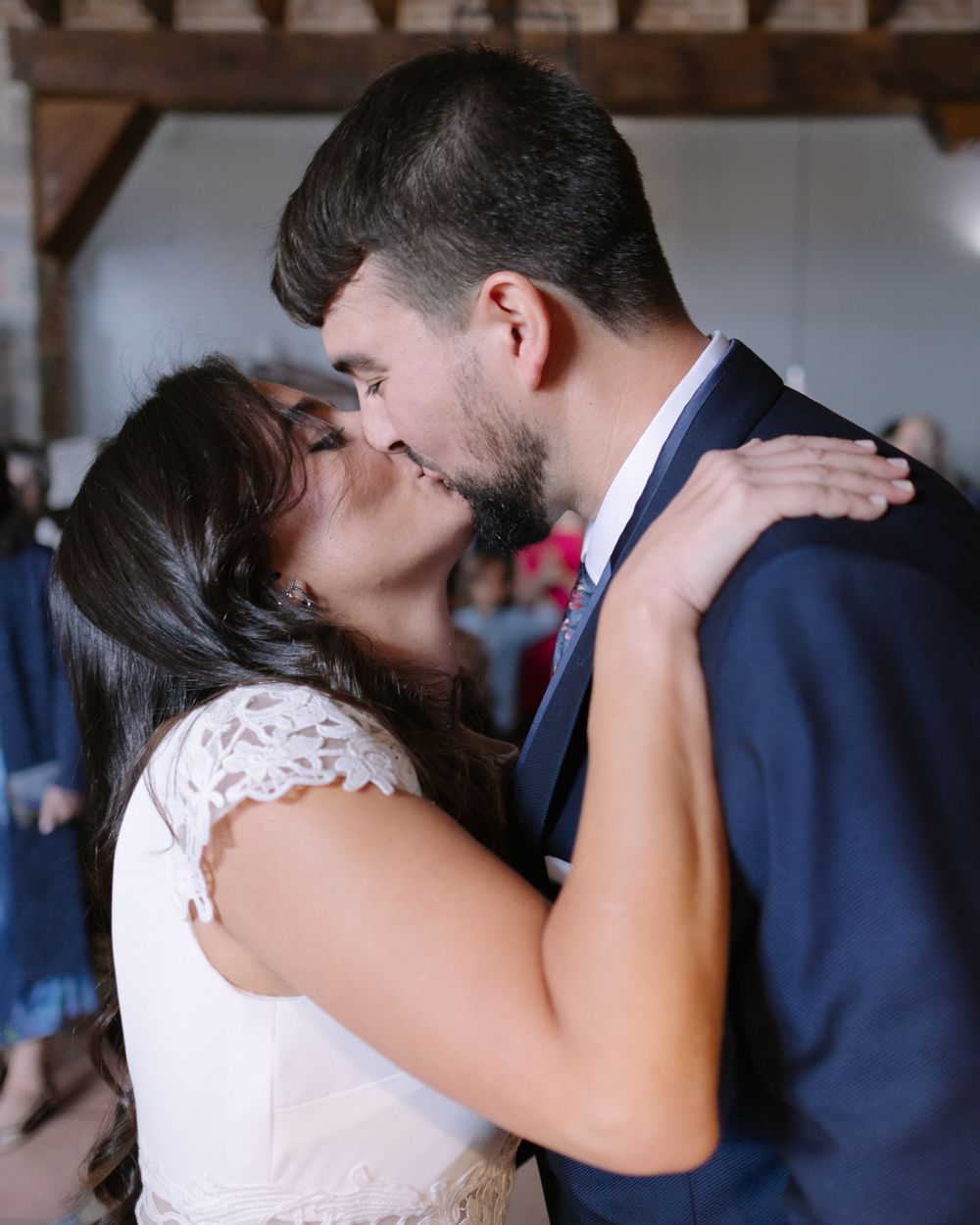 A tender moment between newlyweds sharing a kiss, with the bride in white lace and groom in navy suit.