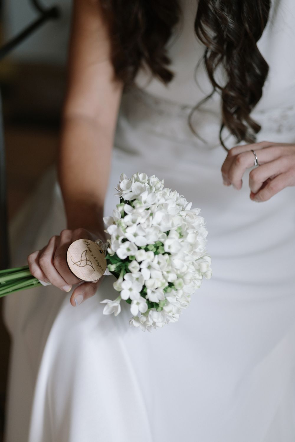 Close-up of a white floral bouquet held against an elegant white wedding dress.