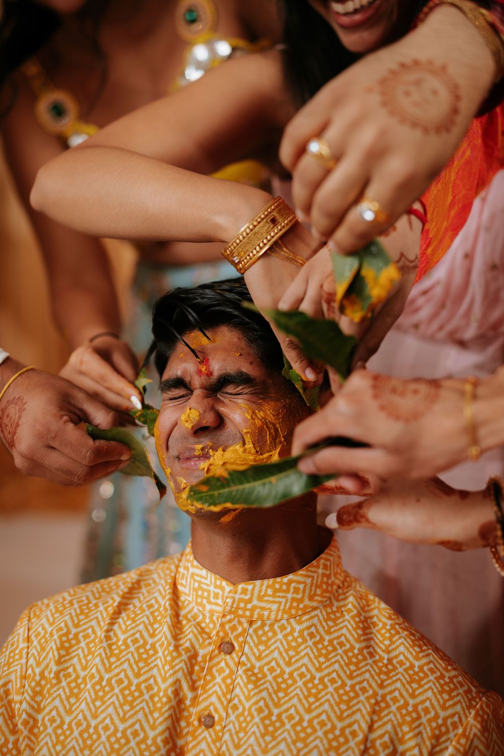 Traditional Indian ceremony showing turmeric application ritual during pre-wedding celebrations with yellow fabric.