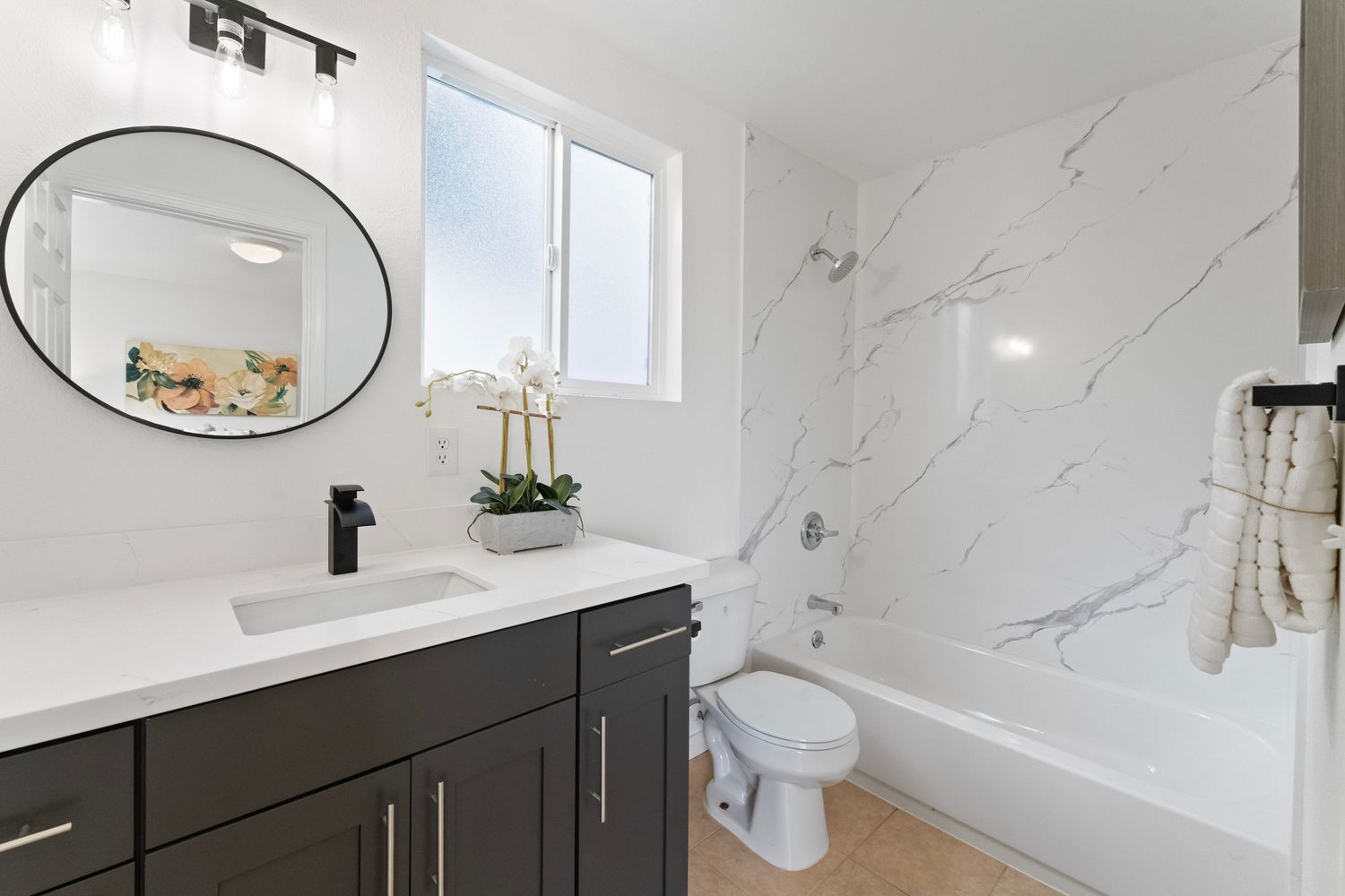 Modern bathroom with marble tile walls, black vanity cabinets, and white countertops features elegant pendant lighting.