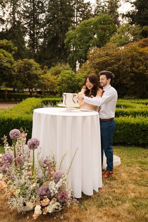 A couple at an outdoor table with floral arrangements celebrates a special occasion in a garden setting.