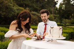 Two people share an intimate moment at a round table decorated with white linens outdoors.