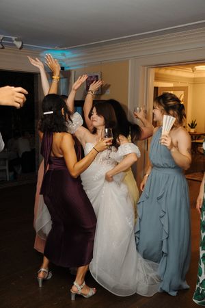 A group of people dancing and celebrating at a wedding reception in formal attire under blue lighting.