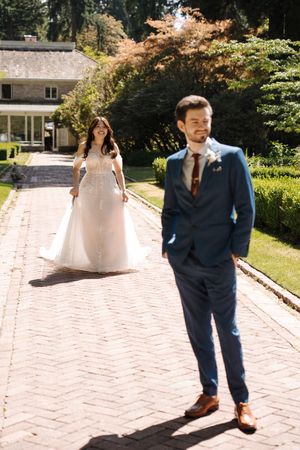 A wedding couple standing on a brick path surrounded by lush greenery and autumn trees on a sunny day.
