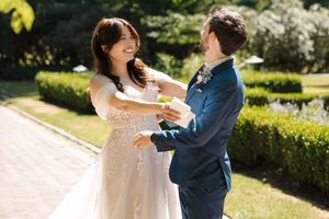 A couple in wedding attire share a romantic dance together in a sunny garden setting.