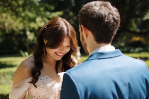 A joyful couple shares a candid moment outdoors in a sunlit garden setting during their wedding celebration.