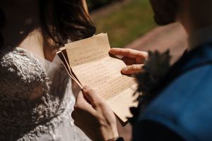 Someone wearing white lace reads a vintage letter in warm sunlight, creating a romantic and nostalgic atmosphere.