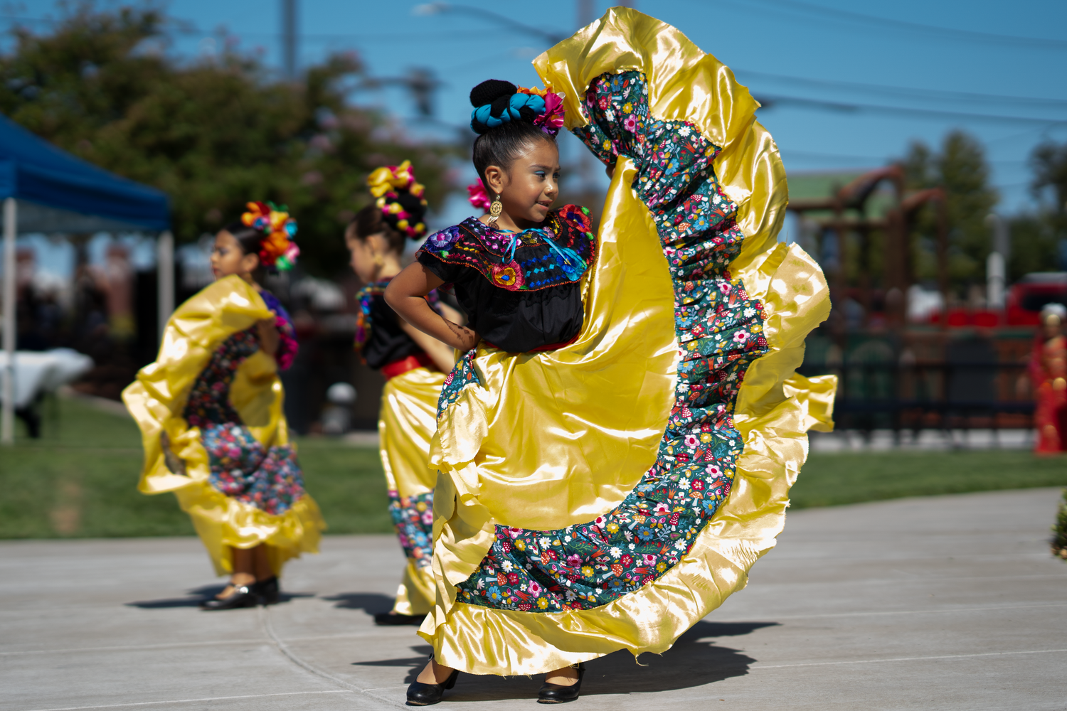 Dancers in flowing yellow skirts perform traditional Mexican folk dances outdoors.